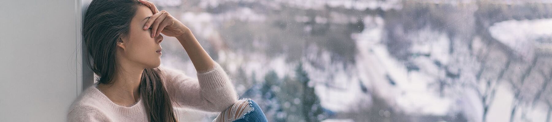 Foto: traurige Frau am Fenster mit Blick auf eine Winterlandschaft