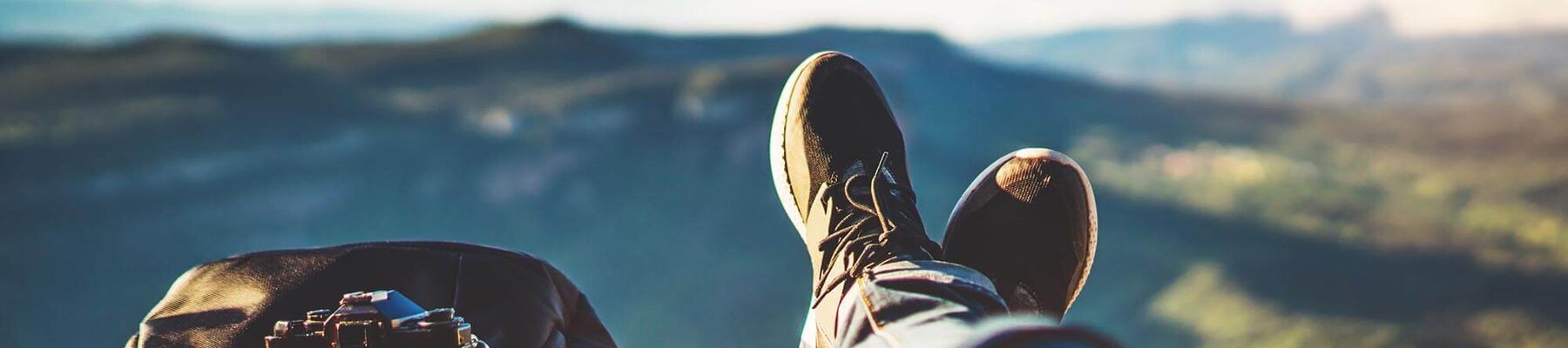 Foto: Wanderschuhe mit Rucksack, Kamera und Tasse vor Bergpanorama