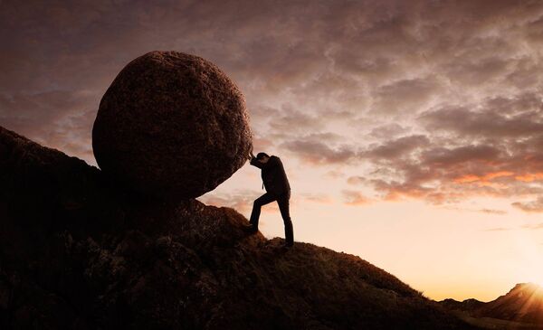 Foto: junger Businessmann schiebt großen Stein bergauf